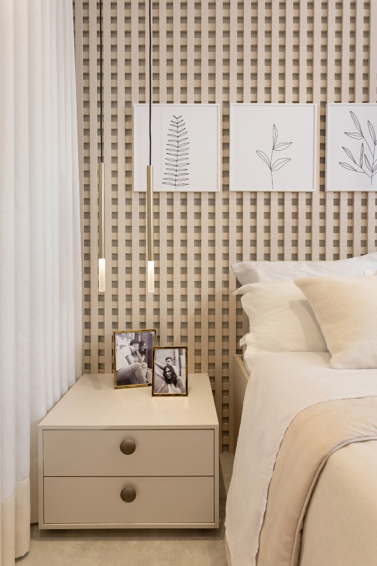 Cabeceira de quarto planejada com nicho em grade de madeira vazada, quadros de linha minimalista com folhagens, pendentes cilíndricos dourados, criado-mudo bege com porta-retratos, cortina de linho branca, roupa de cama bege e caramelo, iluminação quente aconchegante, fotografia de interiores realista
