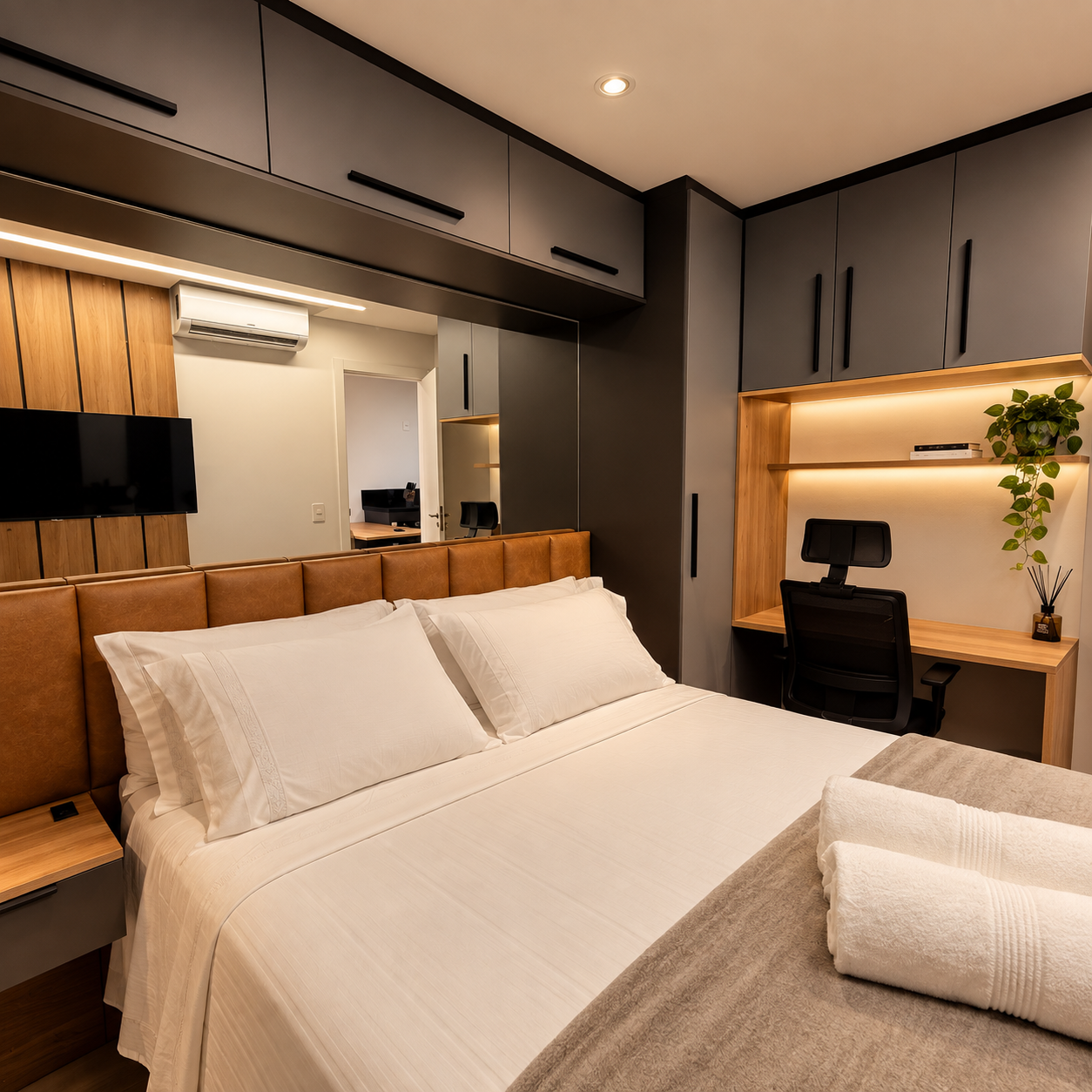 Quarto planejado com marcenaria cinza-chumbo, cabeceira estofada em courino caramelo, escrivaninha com nicho iluminado e cadeira de escritório preta, espelho de parede refletindo ar-condicionado e painel ripado de madeira, fotografia de interiores realista